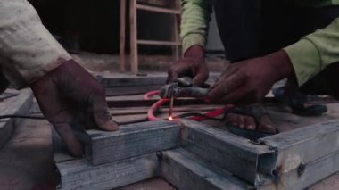 Metal boruları hizalamaya çalışan işçilerin ellerini kapatın. Fabrika atölyesinde demir pencere yapın.