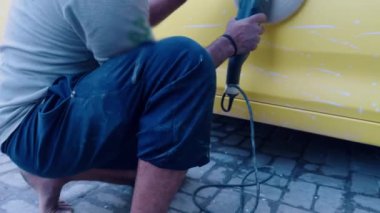 Sarı bir arabayı elektrikli tampon ile cilalarken, dış arabayı cilalarken, atölyede...