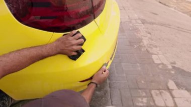Adam, araba atölyesinin arka tarafına odaklanmış bir sünger ve kova suyla boyamadan önce sarı bir spor arabayı elle yıkıyor.