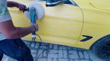 Sarı bir arabayı elektrikli tampon ile cilalarken, dış arabayı cilalarken, atölyede...