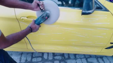 Sarı bir arabayı elektrikli tampon ile cilalarken, dış arabayı cilalarken, atölyede...