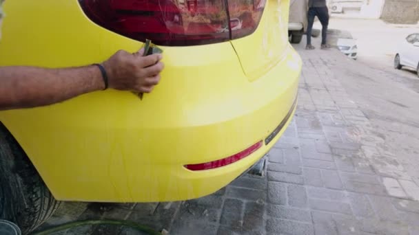 男子手洗一辆黄色跑车 然后用海绵和一桶水在汽车维修车间后侧进行粉刷 — 图库视频影像