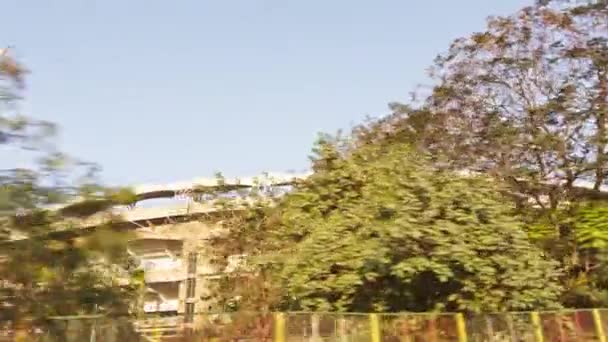 在亚洲的高速公路上开车时 一个现代体育场的外景 在清澈的天空中 有一个巨大的桅杆 周围环绕着绿叶 — 图库视频影像