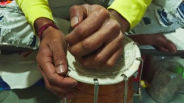 Düzensiz bir masada geleneksel bir davulu akort eden kişi elleri ve enstrüman tamircisiyle ilgilenir. Asya, Hindistan 'daki müzik atölyesinde davul tamir eder.