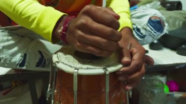 Düzensiz bir masada geleneksel bir davulu akort eden kişi elleri ve enstrüman tamircisiyle ilgilenir. Asya, Hindistan 'daki müzik atölyesinde davul tamir eder.