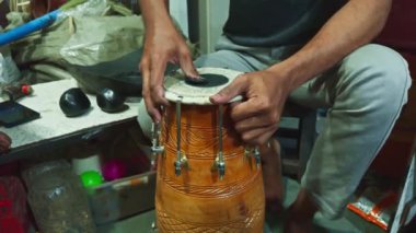 Düzensiz bir masada geleneksel bir davulu akort eden kişi elleri ve enstrüman tamircisiyle ilgilenir. Asya, Hindistan 'daki müzik atölyesinde davul tamir eder.