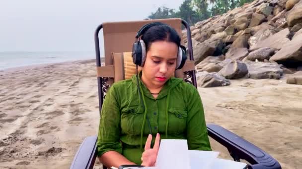 Donna Concentrata Che Legge Libro Sulla Spiaggia Mentre Indossa Cuffie — Video Stock