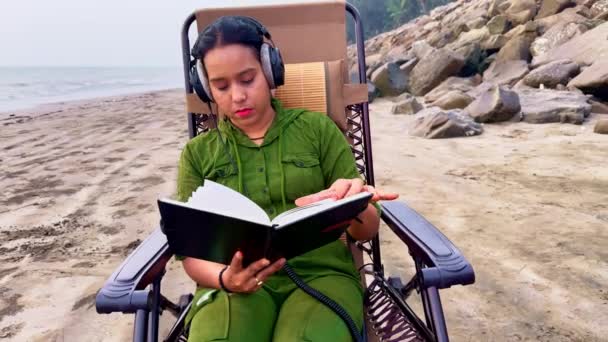 Mulher Focada Lendo Livro Praia Enquanto Usava Fones Ouvido Sentados — Vídeo de Stock