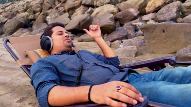 Mężczyzna Relaksujący Się Krześle Plażowym Słuchający Muzyki Słuchawkami Zamkniętymi Oczami — Wideo stockowe
