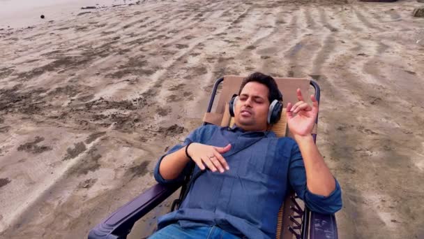 해변에서 평화로운 순간을 즐기는 헤드폰 음악을 해변의 자에서 휴식을 취하는 — 비디오