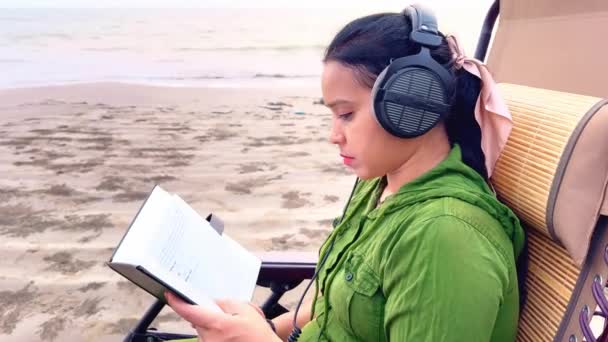 Fókuszált Olvas Egy Könyvet Strandon Miközben Fejhallgatót Visel Fotelben Sziklák — Stock videók