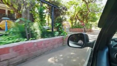 Bir arabanın penceresinden gelen bulanık hareket görüntüsü ağaçları ve tuğla bir duvarı gösteriyor.