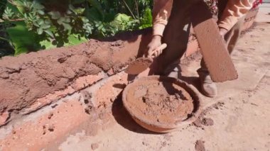 İnşaat duvarı için mala kullanan işçiler taze çimentoyla sıvanmış, aletle ele odaklanmış.