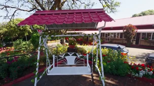 Urocza Huśtawka Ogrodowa Czerwonym Dachem Otoczona Kolorowymi Kwiatami Słonecznym Plenerze — Wideo stockowe