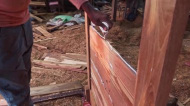 Kırsal bir ahşap atölyesinin açık kapısından etrafa saçılmış ahşap parçaları ve aletlerle insan odundan kapı yapıyor, Asya, Hindistan