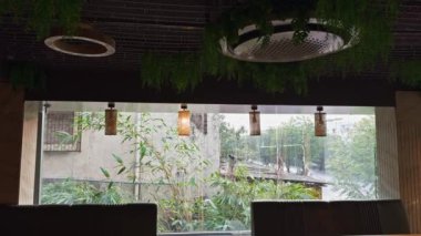 Yeşil duvarları, çiçekli duvar kağıtları, asılı bitkileri, ahşap sandalyeleri ve sıcak bir ortam için hazırlanan masaları olan rahat bir kafe. Asya, Hindistan.  