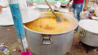 Bir adam açık havada büyük bir tencerede yemek pişiriyor ahşap kaşık, canlı renkler, büyük etkinlik veya geleneksel evlilik için açık hava yemekleri, Asya ve Hindistan ile karıştırılıyor.