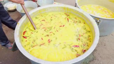 Bir adam açık havada büyük bir tencerede yemek pişiriyor ahşap kaşık, canlı renkler, büyük etkinlik veya geleneksel evlilik için açık hava yemekleri, Asya ve Hindistan ile karıştırılıyor.