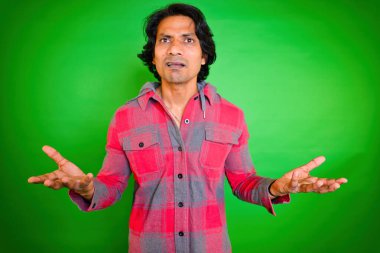 Kafası karışmış bir adam, kafası karışmış bir adam, kafası karışmış, Hintli, şaşkın, uzun saçlı, yeşil arka planda kırmızı ekose gömlek giyen, bilgisiz bir duruş içinde, elleri havada, 30 'lu yaşlarda..