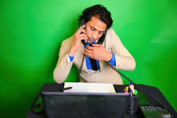 stock image Businessman multitasking with phones and documents, A man juggled at desk, Talking on two phones, While looking at document, Wearing a beige suit blue shirt, with a green background, Indian, juggling.