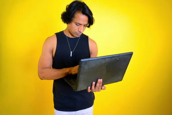 Adam elinde tuttuğu dizüstü bilgisayara dikkatle bakıyor, Laptop kullanan, uzun saçlı, sarı arka planda duran, işkolik, bilgisayarlı, stüdyoda çalışan, Hintli, Asyalı...,