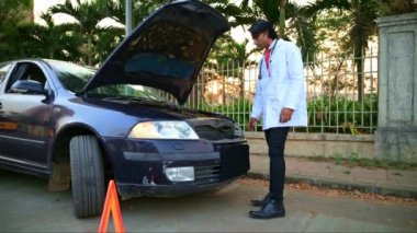 Steteskoplu genç Hintli doktor şehirde yolda kaputu açık bozuk arabaları kontrol ediyor.         