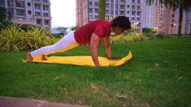 Genç Hintli bir adam parkta sarı minder üzerinde şınav çekiyor, sağlıklı yaşam tarzı konsepti.         