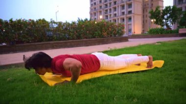 Genç Hintli bir adam parkta sarı minder üzerinde şınav çekiyor, sağlıklı yaşam tarzı konsepti.         