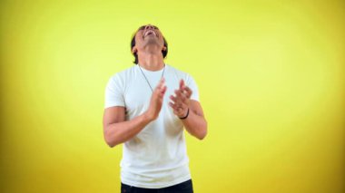 Alkışlayan ve gülen adam, alkışlarla ayakta duran adam, tutkuyla gülen genç adam, mutlu bir duygu taşıyan erkek, heyecanlı bir ifade, beyaz bir tişört içinde, sarı arka plana karşı, Hintli.