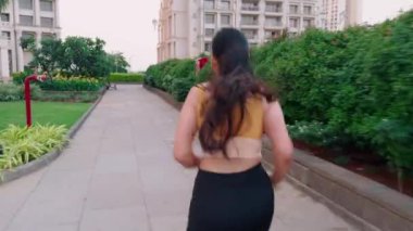 Sarı spor sutyen ve siyah tayt giyen bir kadın parkta koşuyor, yolda koşan bir kız, genç Hintli bir bayan koşucu.            