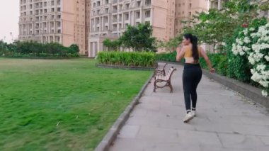 Sarı spor sutyen ve siyah tayt giyen bir kadın parkta koşuyor, yolda koşan bir kız, genç Hintli bir bayan koşucu.            