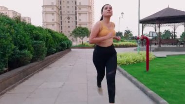 Sarı spor sutyen ve siyah tayt giyen bir kadın parkta koşuyor, yolda koşan bir kız, genç Hintli bir bayan koşucu.            