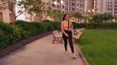 Konut kompleksinde yürüyen bir kadın, patikada yürüyen genç bir bayan, yoga minderiyle yürüyen bir kız sporcu.  