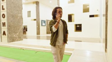 Lobide nöbetteki genç adam, 20 'li yaşlarda Hintli bir apartman koridorunda cep telefonuyla konuşan adam..