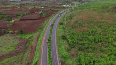 Otoyol üzerinde insansız hava aracı vuruldu, otobanın havadan görünüşü yemyeşil arazide, arka planda tepeler olan bir yerden geçiyor, yol yeşil ve kahverengi toprak parçalarıyla çevrili, Hindistan.
