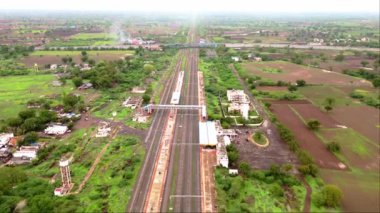 Demiryolu raylarının üzerindeki karayolu, Hindistan 'daki yeşil alanlar ve kırsal binalarla çevrili otoban trafiği görüntüsü. 