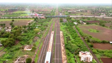 Demiryolu raylarının üzerindeki karayolu, Hindistan 'daki yeşil alanlar ve kırsal binalarla çevrili otoban trafiği görüntüsü. 