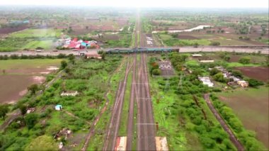 Demiryolu raylarının üzerindeki karayolu, Hindistan 'daki yeşil alanlar ve kırsal binalarla çevrili otoban trafiği görüntüsü. 