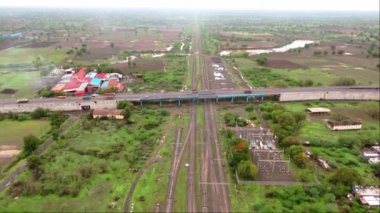 Demiryolu raylarının üzerindeki karayolu, Hindistan 'daki yeşil alanlar ve kırsal binalarla çevrili otoban trafiği görüntüsü. 