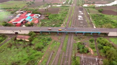 Demiryolu raylarının üzerindeki karayolu, Hindistan 'daki yeşil alanlar ve kırsal binalarla çevrili otoban trafiği görüntüsü. 