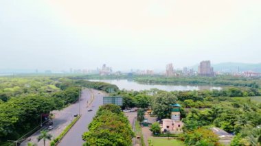 Göl kenarındaki bir otoyolun hava görüntüsü, insansız hava aracı Mumbai şehir manzarası, çevresindeki yemyeşil ve şehir binaları, arka planda yüksek kuleler, göle paralel giden trafik, Hindistan