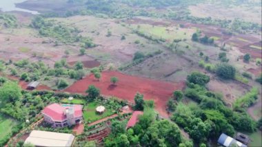 Yeşilliklerle çevrili küçük bir kasaba, kırmızı topraklı tarım arazisi, arka planda nehir gölü, Uzak tepeler, Hindistan