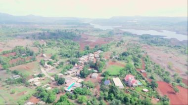 Yeşilliklerle çevrili küçük bir kasaba, kırmızı topraklı tarım arazisi, arka planda nehir gölü, Uzak tepeler, Hindistan