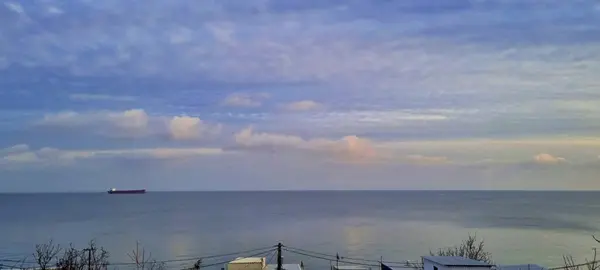The ship is moving along the horizon.The clouds are beautifully reflected on the smooth sea surface.