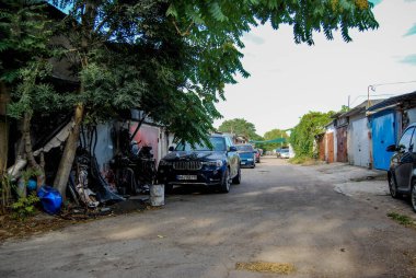 Private vehicles are parked in the alley of the garage complex. A beautiful blue BMW X3 crossover stands next to a pile of automobile garbage. clipart