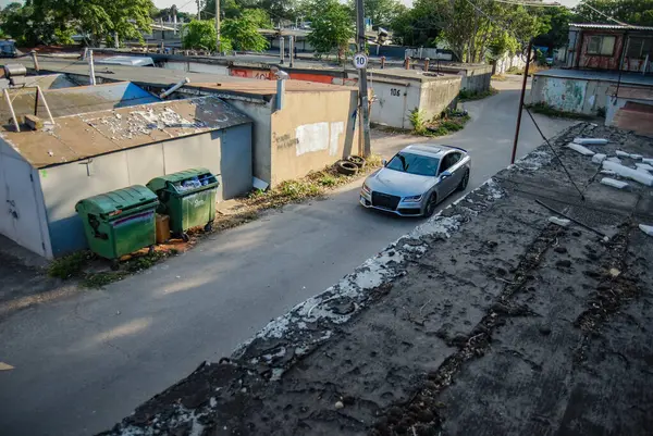 Garaj kompleksinin geniş bir alanı, yukarıdan görünüyor. Garaj kompleksinin caddesinde gümüş renkli bir Audi A7 sürüyor..