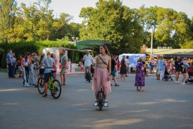 Odessa parkında dinlenen bir sürü insan var. İnsanlar parkta yürüyor, bisiklete biniyor, tek tekerlekli bisiklete biniyor ve ayrıca eğlence etkinlikleri de var..