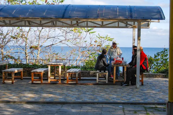 Deniz kenarında çardak. Güneşli bir sonbahar gününde, bir grup insan deniz kenarında sohbet eder..