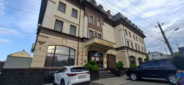 Güzel yol kenarı oteli. Kremalı, kahverengi perili ve dikdörtgen pencereli üç katlı bir bina. Büyük kemerli girişte 