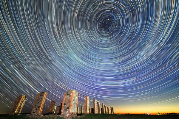 Uzun pozlu bir çekim, Smiltenes Stounhedza harabelerinin üzerinde daireler çizen büyüleyici yıldız izlerini yakalar. Antik taş yapılar yıldızların canlı renkleriyle berrak, gece gökyüzünün zeminine karşı dimdik dururlar.. 